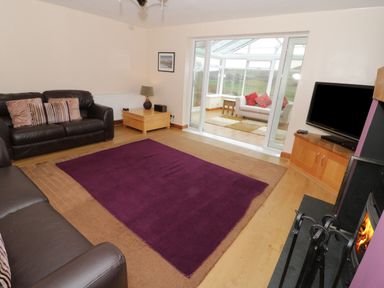 A living room with two leather sofas a wooden coffee table a purple rug and a television next to a fireplace at Bryn Derw Holiday Cottage in Eglwysbach near Llanrwst and Conwy