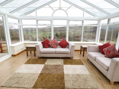 A conservatory with two sofas and a checkered rug at Bryn Derw Holiday Cottage Eglwysbach near Llanrwst and Conwy
