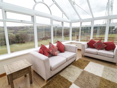 A sunroom with two sofas and a wooden side table at Bryn Derw Holiday Cottage in Eglwysbach near Llanrwst and Conwy