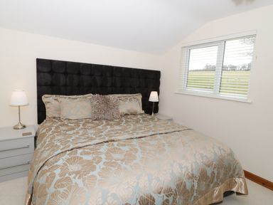 A bedroom with a large bed with patterned bedding two bedside tables with lamps and a window with blinds at Bryn Derw Holiday Cottage Eglwysbach near Llanrwst and Conwy