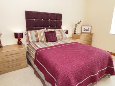 A bedroom with a bed with a purple headboard and bedspread flanked by wooden bedside tables with lamps at Bryn Derw Holiday Cottage in Eglwysbach near Llanrwst and Conwy