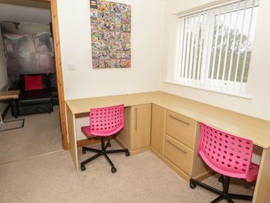 A corner office space with a wooden desk two pink swivel chairs a window with vertical blinds and comic book wall art at Bryn Derw Holiday Cottage Eglwysbach near Llanrwst and Conwy