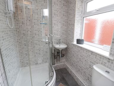 A bathroom with a shower enclosure a small wall mounted sink a toilet and a frosted window at Bryn Derw Holiday Cottage in Eglwysbach near Llanrwst and Conwy