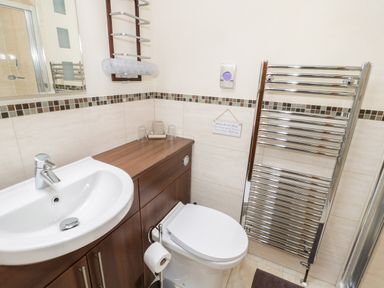 A bathroom with a white sink, wooden vanity, white toilet, towel rack, and a small sign on the wall at Bryn Derw Holiday Cottage Eglwysbach near Llanrwst and Conwy