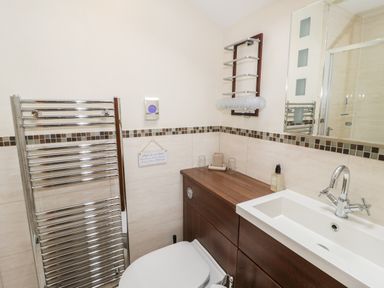 A bathroom with a white sink, wooden cabinet, toilet, chrome towel radiator, wall-mounted glass holder and a large mirror at Bryn Derw Holiday Cottage Eglwysbach near Llanrwst and Conwy