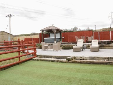 An outdoor patio area with two lounge chairs a table with four chairs a wooden gazebo with a hot tub surrounded by a red wooden fence Bryn Derw Holiday Cottage Eglwysbach near Llanrwst and Conwy
