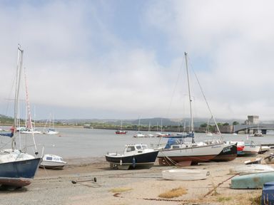 A riverside with various boats docked on the shore and moored in the water near a stone bridge at Bryn Derw Holiday Cottage Eglwysbach near Llanrwst and Conwy