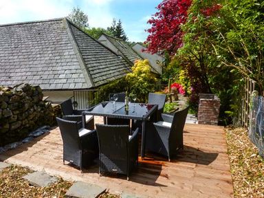 An outdoor patio with a black glass table and six black chairs surrounded by plants and a stone wall at The Nook in Bowness-On-Windermere