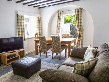 A living room with a sofa and ottoman near a dining table with chairs at The Nook in Bowness-On-Windermere