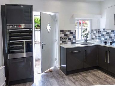 A kitchen with black cabinets a double oven a sink and a partially open door at The Nook in Bowness-On-Windermere