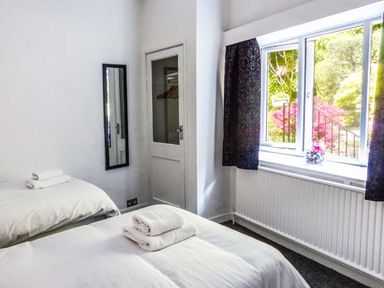 A bedroom with two single beds towels on beds a mirror on the wall and a window with dark curtains at The Nook in Bowness-On-Windermere