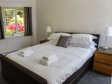 A bedroom with a bed with white bedding and towels on it two bedside tables with lamps and a window with curtains at The Nook in Bowness-On-Windermere