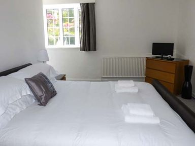A bedroom with a bed white bedding folded towels a window a chest of drawers with a TV and a lamp at The Nook in Bowness-On-Windermere