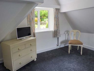A small room with a chest of drawers and a television next to a window and a single chair on carpeted floor at The Nook in Bowness-On-Windermere