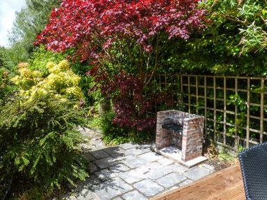 A garden area with stone paving a brick barbecue and various trees and bushes at The Nook in Bowness-On-Windermere