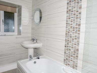A bathroom with a bathtub sink round mirror and a window at The Nook in Bowness-On-Windermere