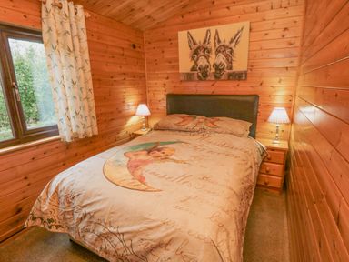 A bedroom with a double bed between two bedside tables with lamps and a window with curtains at Hawthorne Lodge Liverton near Danby