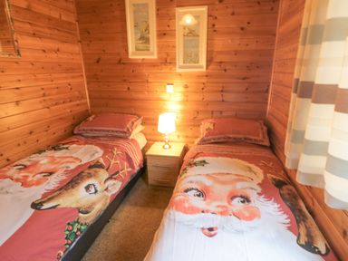 A bedroom with two single beds with Santa and reindeer bedding and a lamp on a nightstand at Hawthorne Lodge in Liverton near Danby