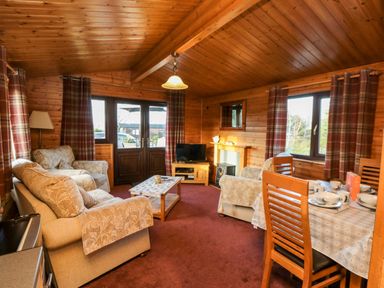A wooden living room with sofas, a coffee table, a television, a dining table set with dishes and cups at Hawthorne Lodge in Liverton near Danby