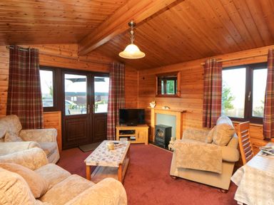 A living room with armchairs a coffee table a television and wooden walls at Hawthorne Lodge in Liverton near Danby