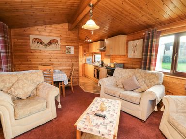 A living room with beige sofas and a wooden coffee table next to a kitchen and dining area at Hawthorne Lodge in Liverton near Danby