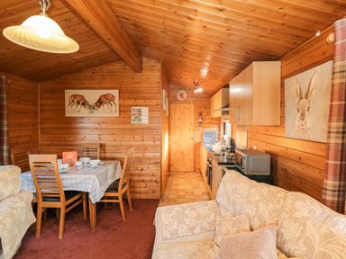 A wooden interior with a dining table set with crockery and a kitchen area with light wood cabinets and appliances at Hawthorne Lodge in Liverton near Danby
