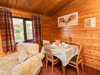 A dining area with wooden chairs and table set for four beside a window with plaid curtains and a beige patterned sofa at Hawthorne Lodge in Liverton near Danby