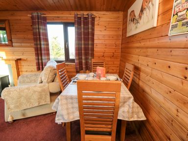 A dining area with a table set for breakfast four wooden chairs and a window with curtains in a wooden cabin at Hawthorne Lodge in Liverton near Danby