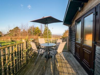A wooden deck with a round table four chairs and an umbrella outside a wooden building at Hawthorne Lodge in Liverton near Danby