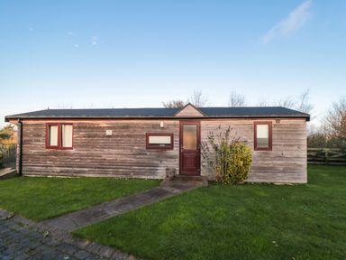 A single-story wooden lodge with three windows and a door surrounded by grass at Hawthorne Lodge in Liverton near Danby