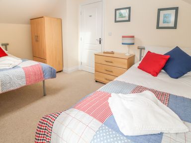 A bedroom with two single beds a wooden wardrobe and a wooden chest of drawers with a lamp at Atlantic Reach in Widemouth Bay