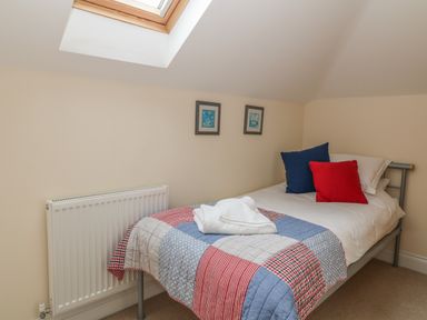 A small bedroom with a single bed with a patchwork quilt and two framed pictures on the wall at Atlantic Reach in Widemouth Bay