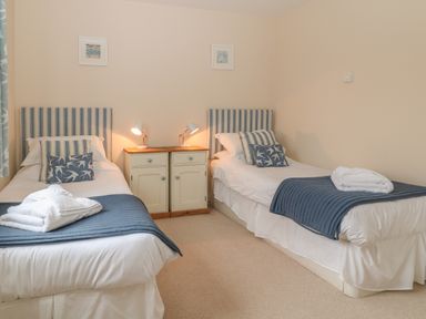 A bedroom with two single beds with striped headboards and blue throws at Atlantic Reach in Widemouth Bay