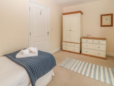 A bedroom with a single bed with folded towels on a blue blanket a white door a white and wooden wardrobe and dresser and a striped rug on the floor at Atlantic Reach in Widemouth Bay