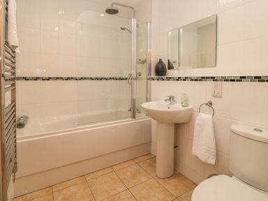 A bathroom with a bathtub shower combination a sink a wall mirror a toilet and a towel ring with a towel at Atlantic Reach in Widemouth Bay