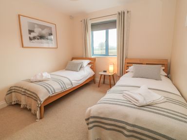 A bedroom with two single beds a window and a framed picture at Atlantic Reach in Widemouth Bay
