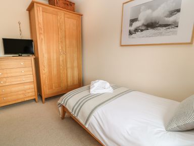 A bedroom with a single bed a striped blanket a pillow wooden wardrobe chest of drawers and a television at Atlantic Reach in Widemouth Bay