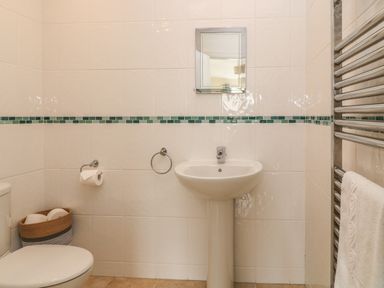 A bathroom with a toilet a pedestal sink a mirror towel rack and a basket with toilet paper rolls at Atlantic Reach in Widemouth Bay