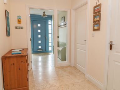 A hallway with a wooden cabinet and blue door with windows at Atlantic Reach in Widemouth Bay