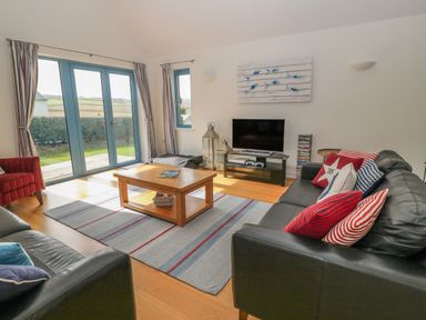 A living room with black leather sofas striped cushions a wooden coffee table television and glass doors at Atlantic Reach in Widemouth Bay