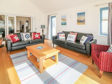 A living room with two black sofas, a red armchair, a wooden coffee table, a rug, and framed beach posters at Atlantic Reach in Widemouth Bay