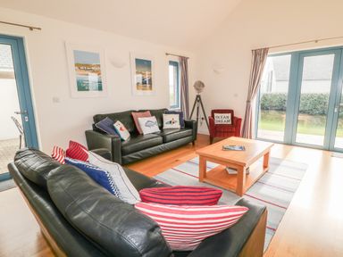 A living room with black leather sofas cushions wooden coffee table and blue doors at Atlantic Reach in Widemouth Bay