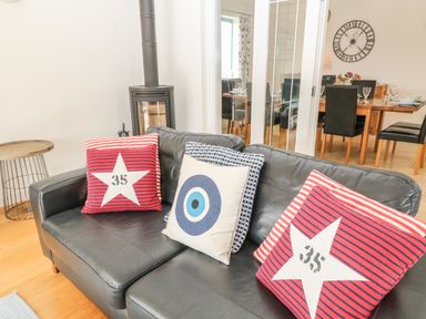 A black leather sofa with three decorative cushions near a wood-burning stove and a wooden side table at Atlantic Reach in Widemouth Bay
