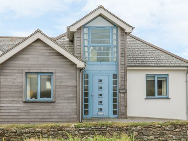 A house with a blue front door and windows stone wall and grass in front at Atlantic Reach in Widemouth Bay