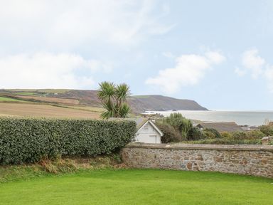 A garden with a hedge and stone wall overlooking fields and coastline at Atlantic Reach in Widemouth Bay