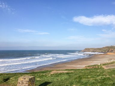 A coastal beach with waves and cliffs in the distance at Atlantic Reach in Widemouth Bay