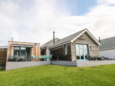 A modern wooden house with outdoor seating and sun loungers on a deck at Atlantic Reach in Widemouth Bay