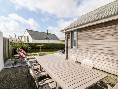 An outdoor patio area with a large dining table and chairs next to a wooden siding house and garden at Atlantic Reach in Widemouth Bay