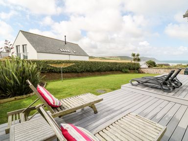 A garden with wooden and plastic lounge chairs on a deck and a house in the background at Atlantic Reach in Widemouth Bay