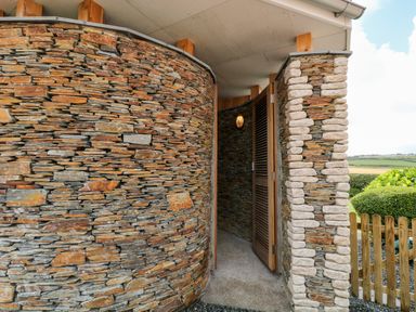 An entrance to a curved stone structure with wooden door and outdoor light at Atlantic Reach in Widemouth Bay